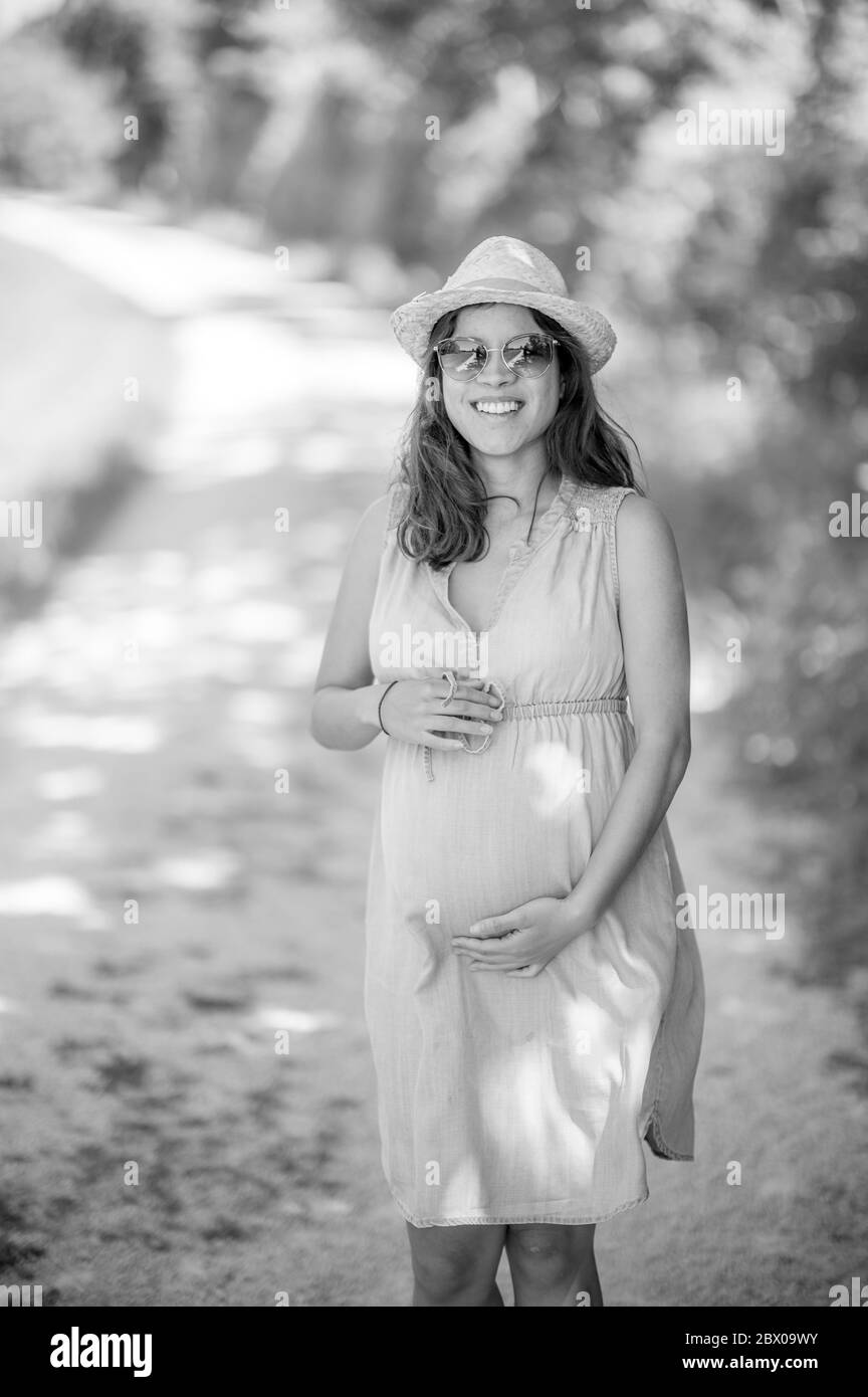 Outdoor-Porträt von glücklichen schwangeren Frau mit Sonnenbrille und Hut - Sommerzeit in der Natur - schöne Momente des Familienlebens Stockfoto