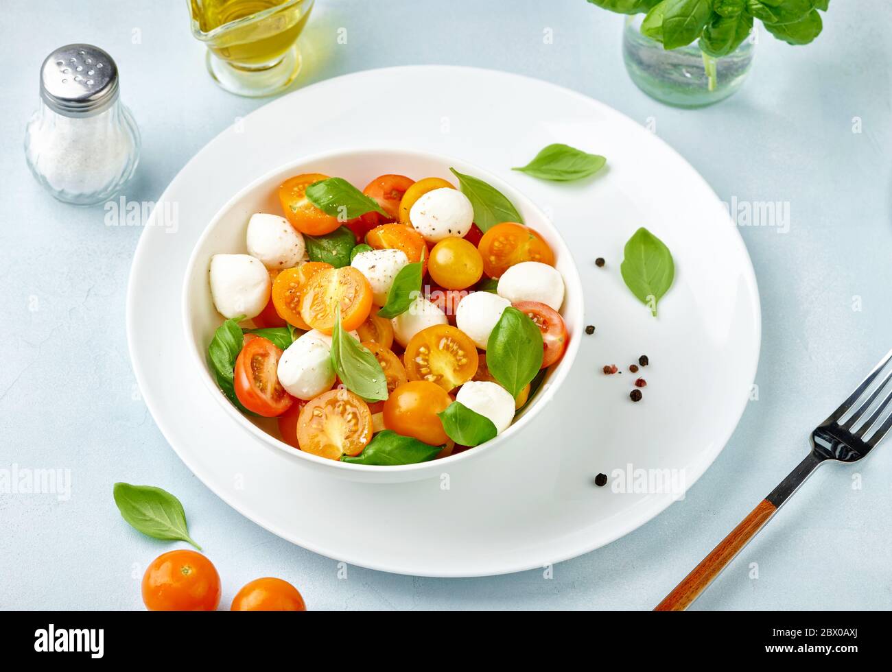 Caprese Salat mit Tomaten und Mini Mozzarella Käse in weißer Schüssel auf weißem Teller. Bocconcini Mozzarella Käse mit Basilikumblättern. Stockfoto
