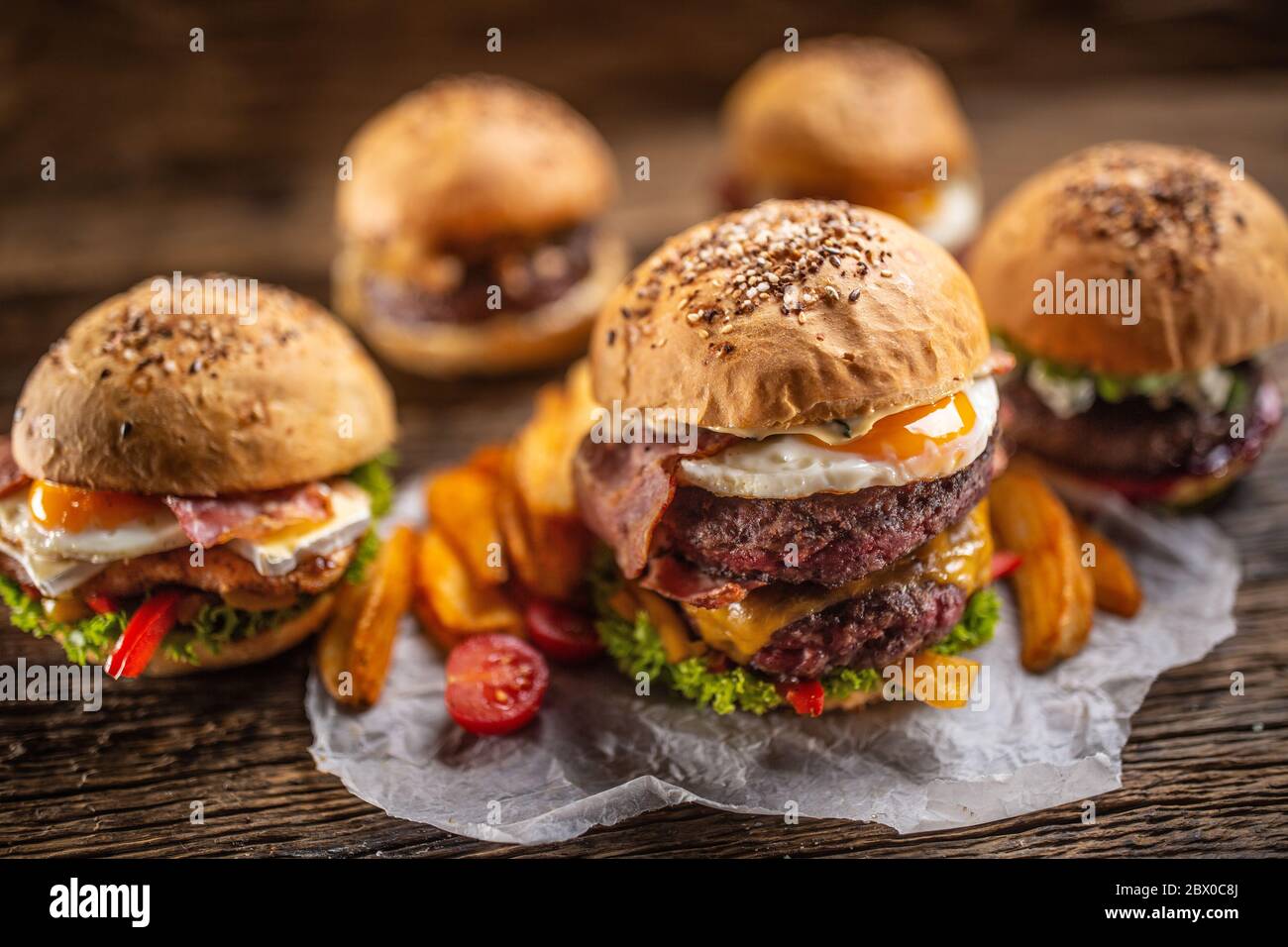 Auswahl an verschiedenen frischen leckeren Burgern mit Kartoffelkeilen in rustikaler Umgebung Stockfoto