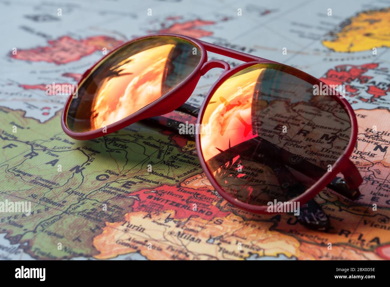 Rote Sonnenbrille mit einem Spiegelbild eines Flugzeugs am Himmel auf einer Karte von europa Stockfoto