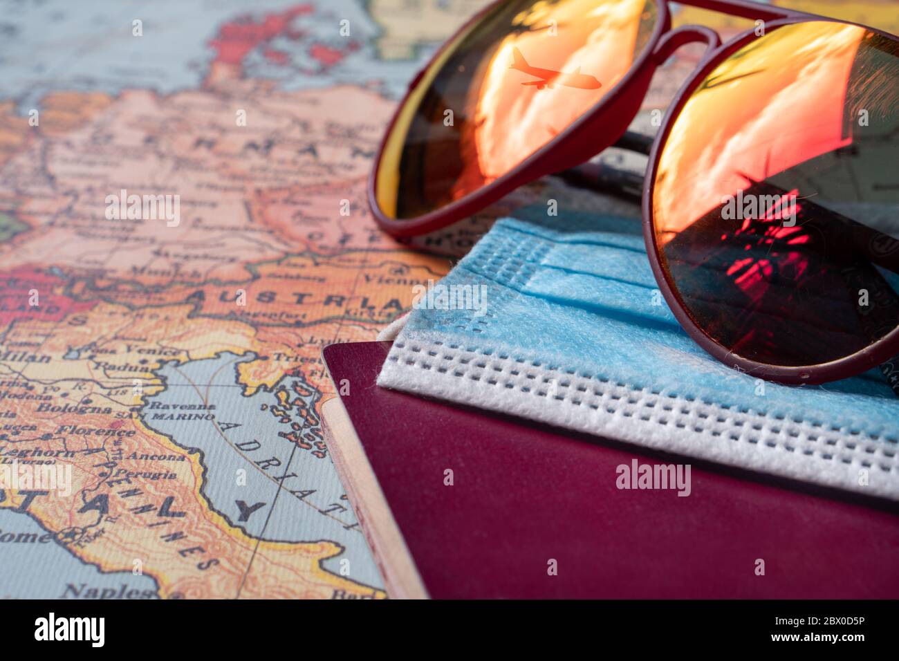 Rote Sonnenbrille mit einem Spiegelbild eines Flugzeugs am Himmel, einer blauen OP-Maske und einem Pass auf einer Europakarte. Konzept des Urlaubs nach dem covid-19 Stockfoto
