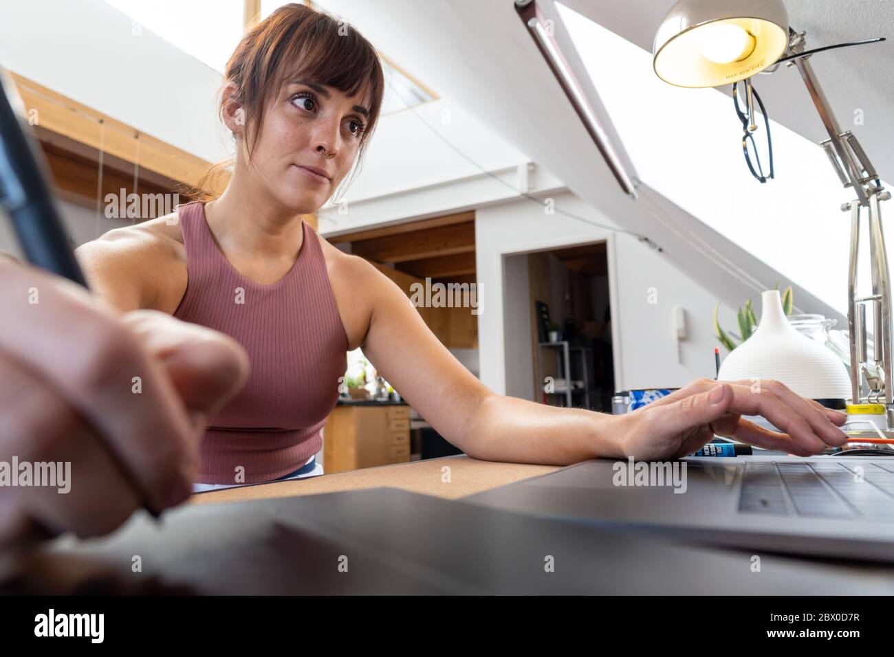 Eine konzentrierte kaukasische Frau mit Piercing arbeitet zu Hause mit dem Laptop und mit einem Grafik-Tablet. Konzept des Home Office während des Coronavirus Stockfoto