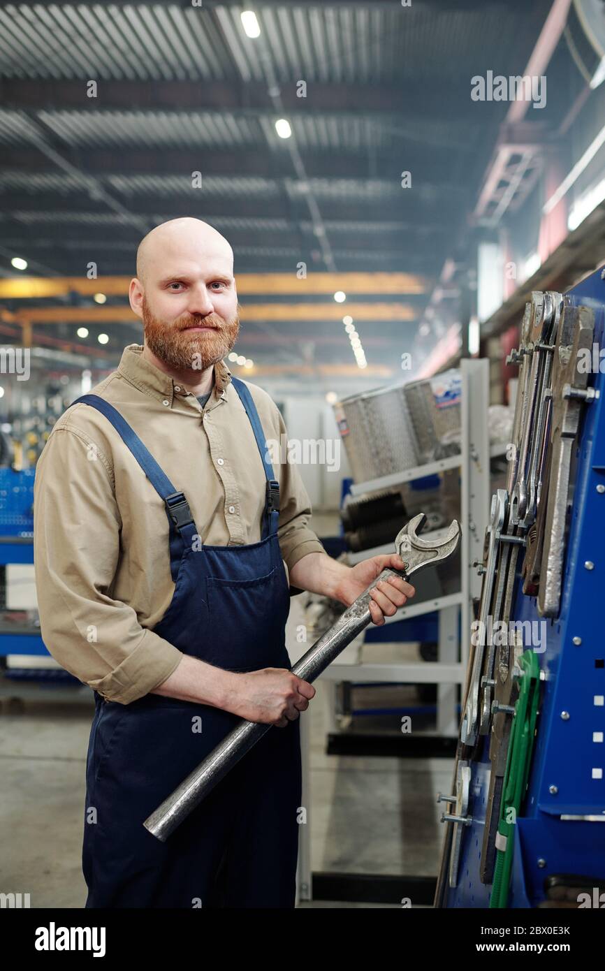 Porträt des kahlen bärtigen Mann mit großen Metallschlüssel und stehend in Industrie-Shop Stockfoto