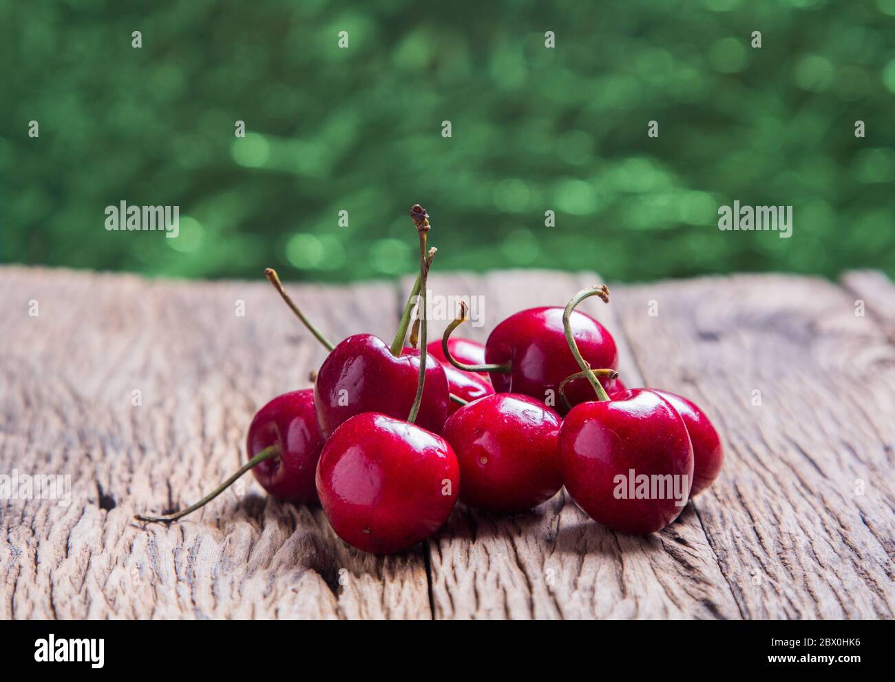 Kirschen auf Holztisch mit abstraktem kreisförmigen grünen Bokeh Hintergrund, Nahaufnahme für Designarbeit Stockfoto