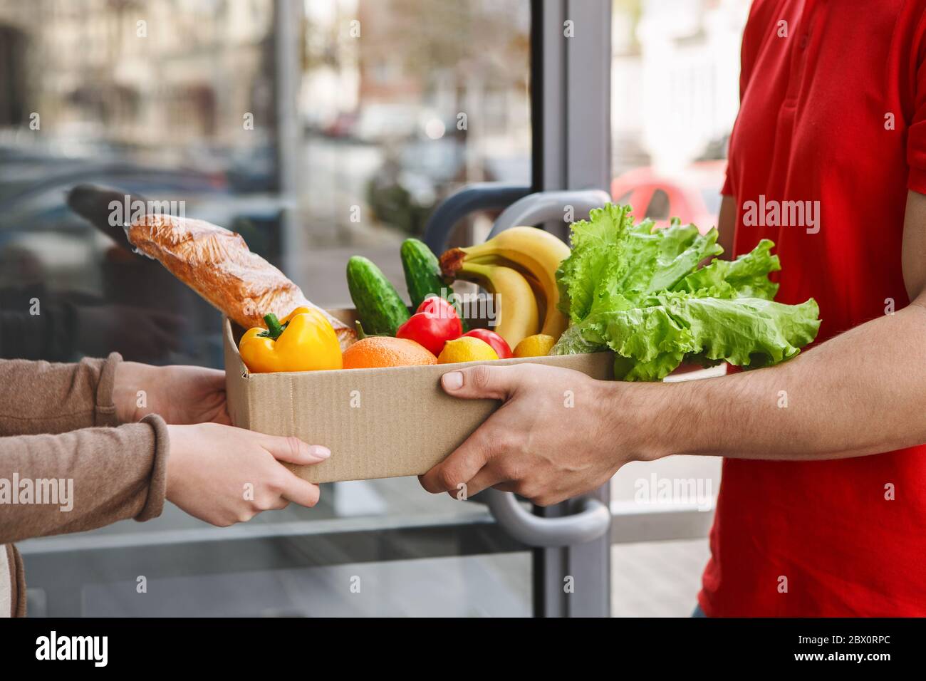 Lebensmittel per Kurier kaufen. Deliveryman gibt Box von Produkten an Mädchen Stockfoto