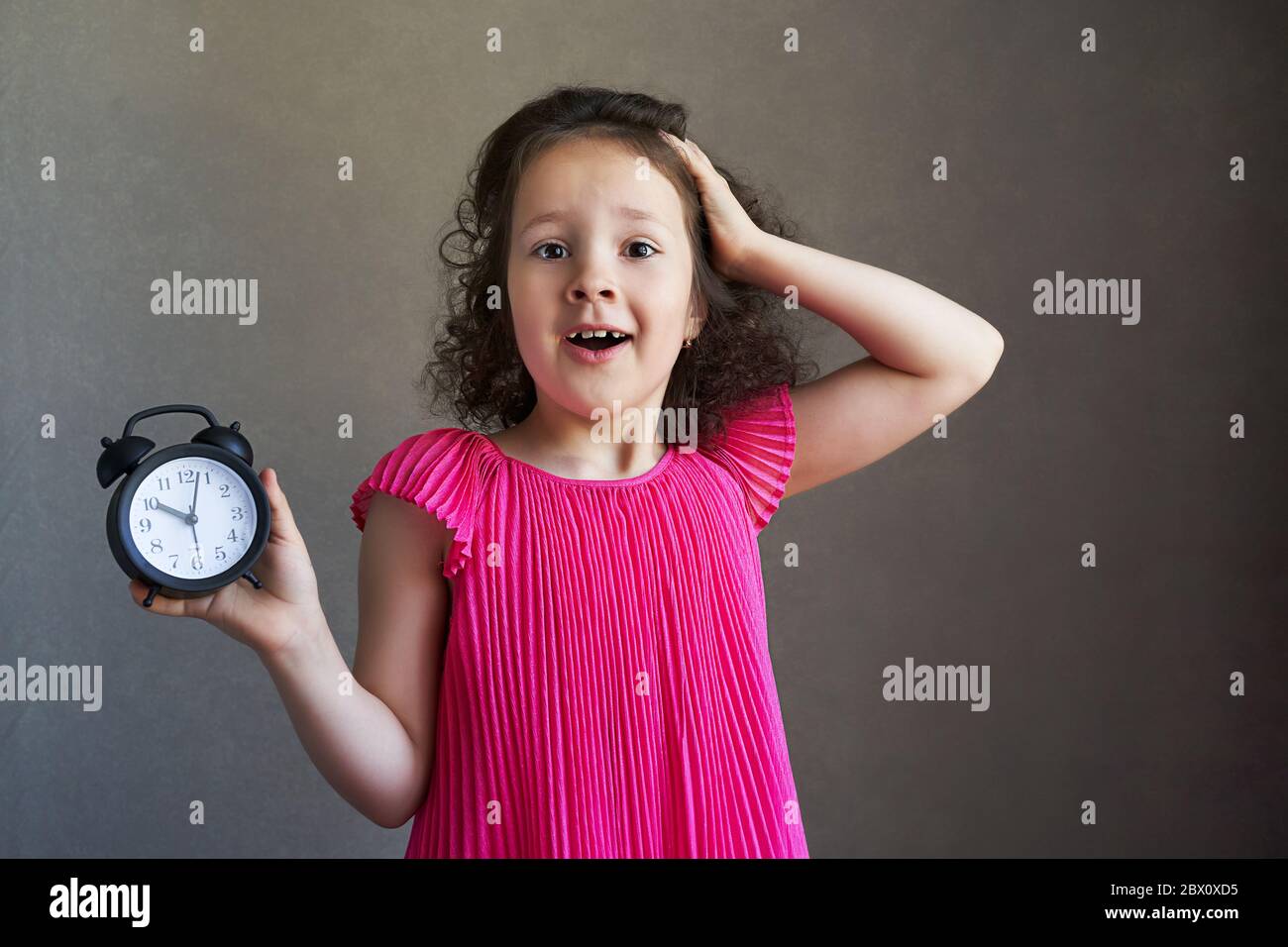 Schöne lockige kleine Mädchen mit einem Schreibtisch Uhr Stockfoto