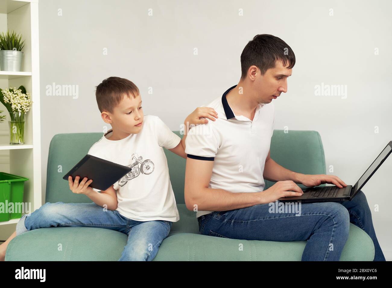 Freiberuflicher Mitarbeiter, der zu Hause unter angenehmen Bedingungen arbeitet. Mann versucht zu arbeiten, Kind verhindert seinen Vater zu arbeiten. Stockfoto