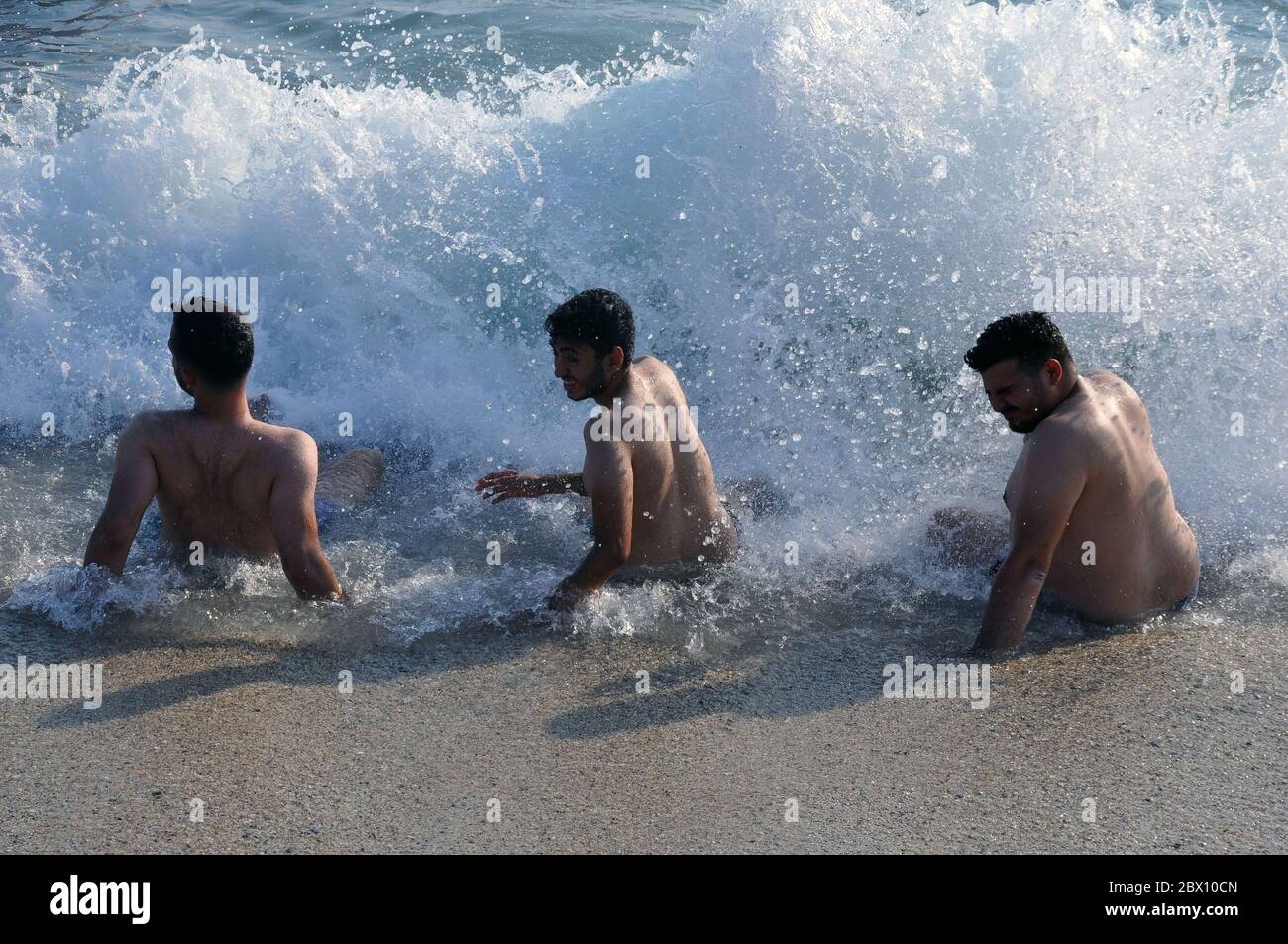 Drei junge Männer sitzen am Meer und fangen Wellen. Stockfoto