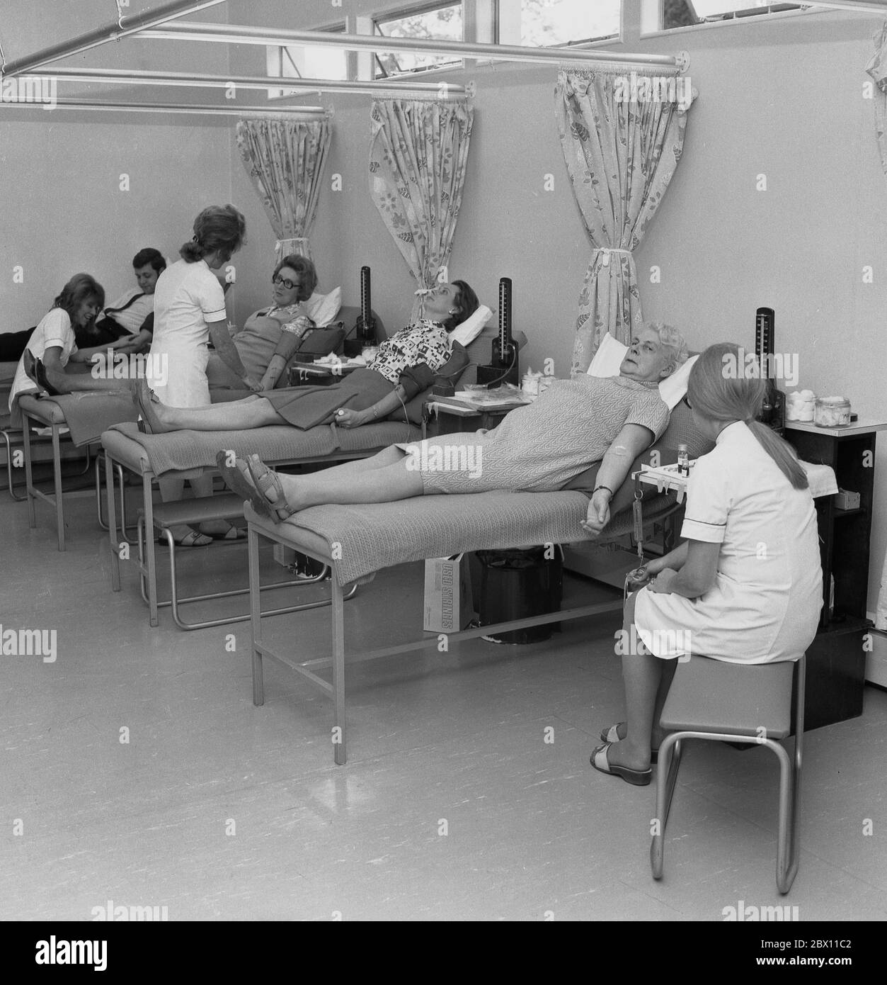 „Blutspender“, Mitglieder der Öffentlichkeit, die in einem medizinischen oder medizinischen Zentrum freiwillig auf chirurgischen Betten liegen und Blut spenden, Lewisham, South London, Ende der 60er, Anfang der 70er Jahre. Blut für die Versorgung der Gemeinschaft zu geben, ist ein öffentlicher Akt, der von Menschen getragen wird, da Blut Leben retten kann. Stockfoto