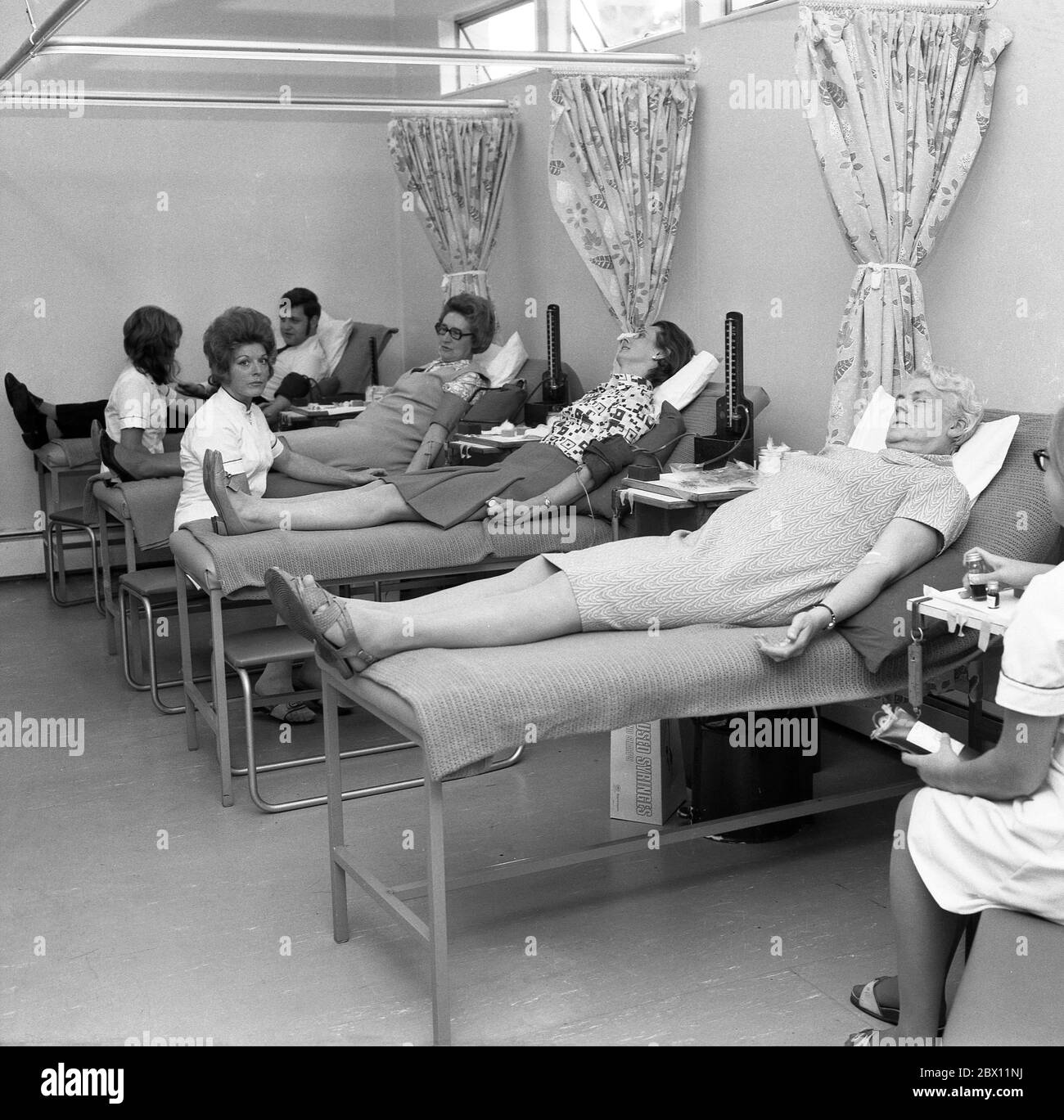 „Blutspender“, Mitglieder der Öffentlichkeit, die in einem medizinischen oder medizinischen Zentrum freiwillig auf chirurgischen Betten liegen und Blut spenden, Lewisham, South London, Ende der 60er, Anfang der 70er Jahre. Blut für die Versorgung der Gemeinschaft zu geben, ist ein öffentlicher Akt, der von Menschen getragen wird, da Blut Leben retten kann. Stockfoto