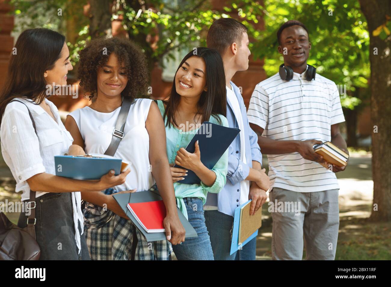 Gruppe multikultureller Studenten, die sich nach dem Unterricht im Freien ausruhen, plaudern und lachen Stockfoto