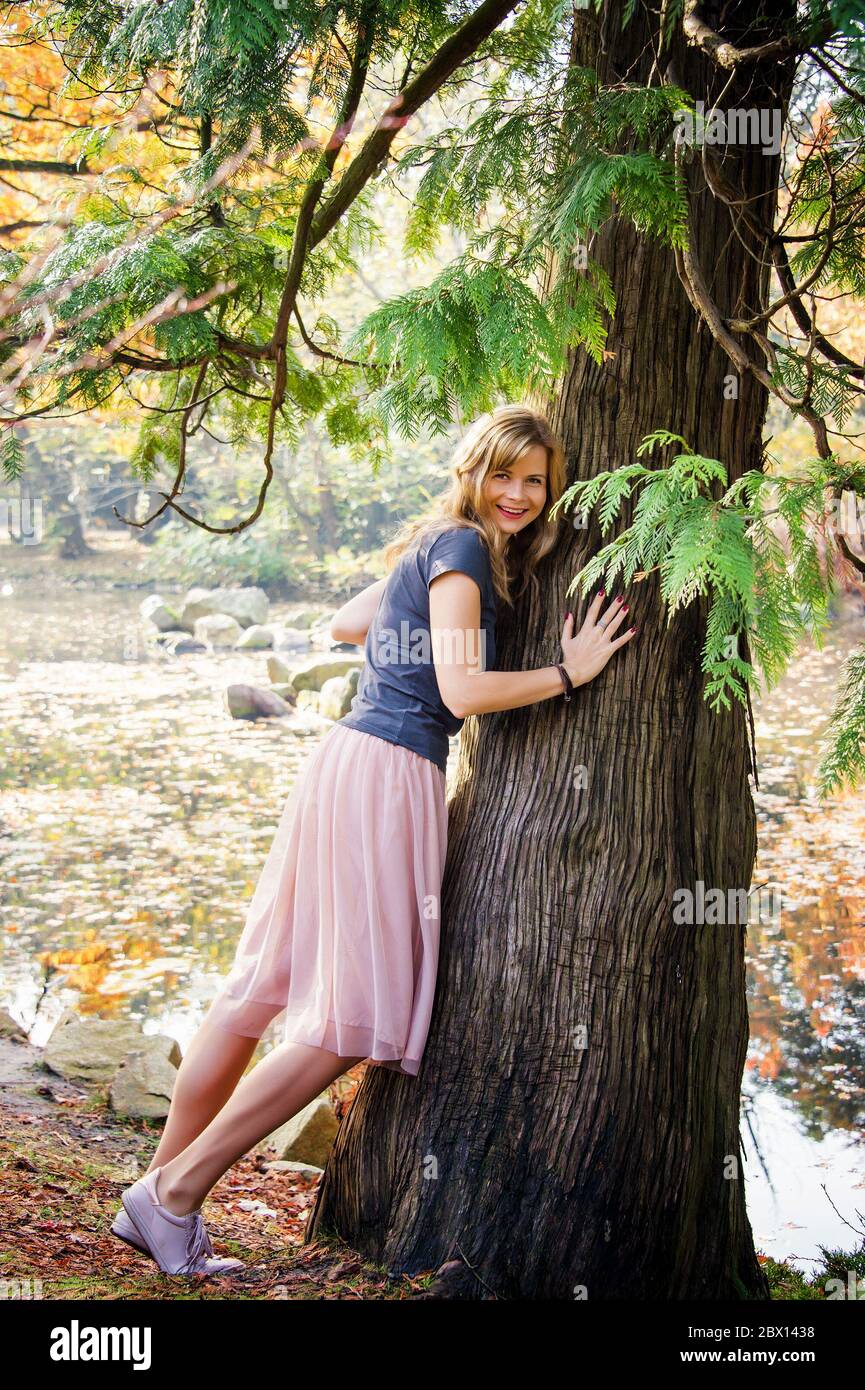 Junge Frau umarmt einen Baum im Herbst Stadtpark Stockfoto