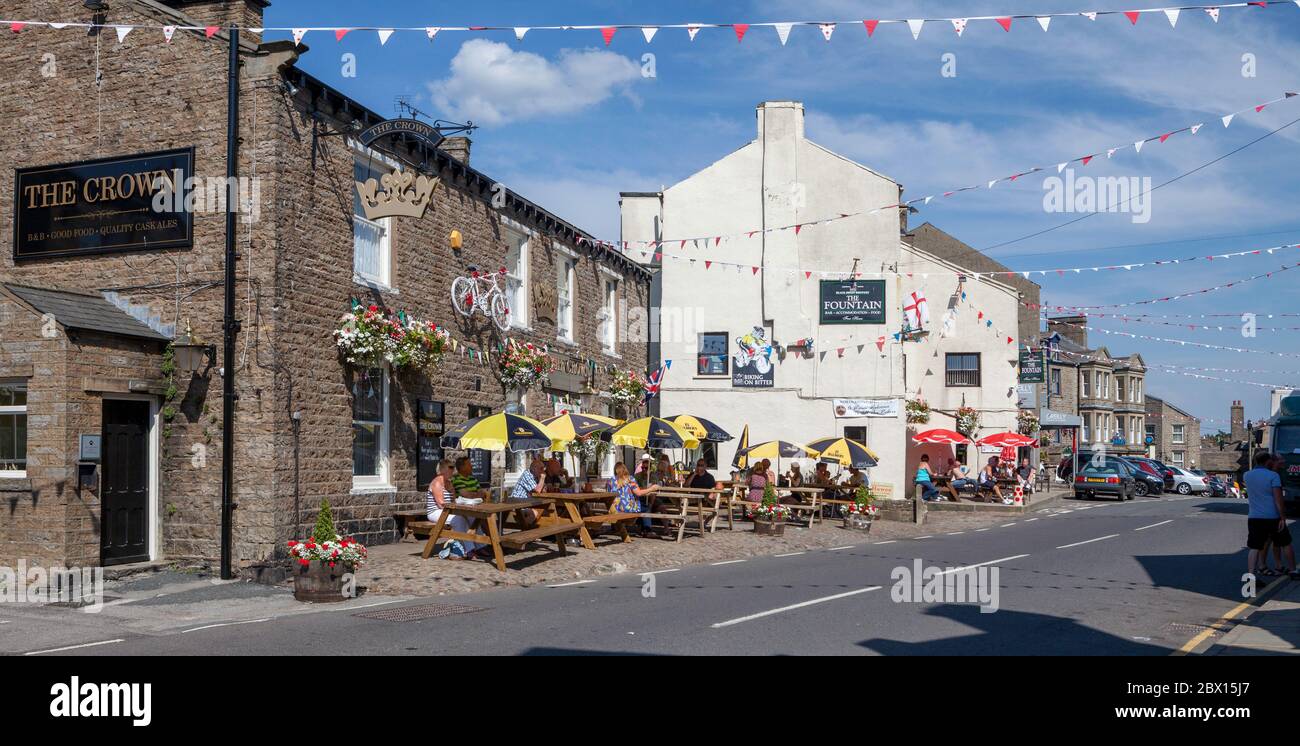 Besucher sitzen an einem sonnigen Sommertag vor den Crown and Fountain Pubs im Zentrum der kleinen Stadt Hawes in Yorkshire Dales Stockfoto