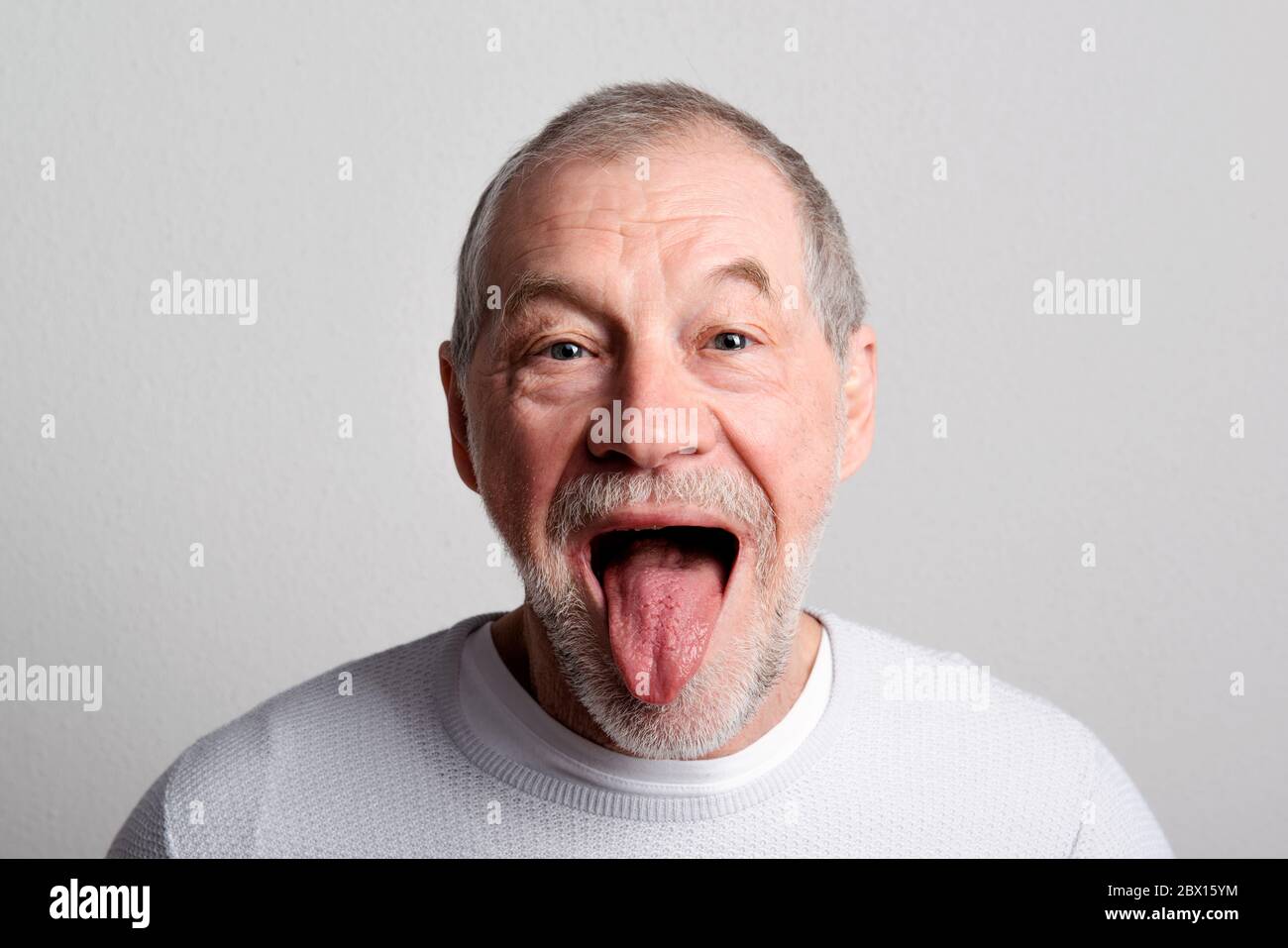Porträt eines fröhlichen älteren Mannes in einem Studio, herausstehende Zunge. Stockfoto