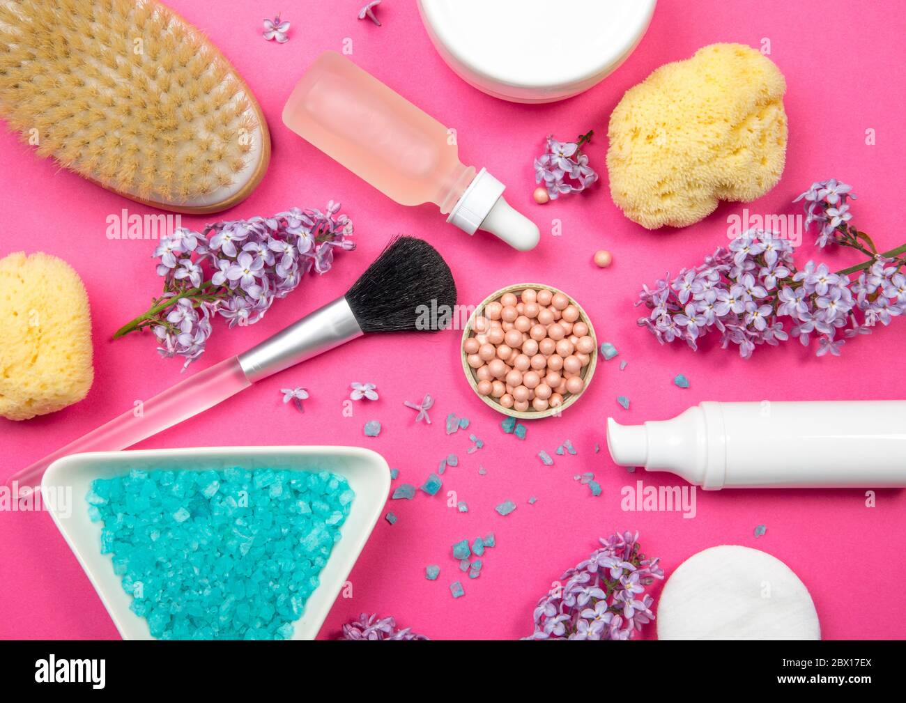 Flache Ansicht von verschiedenen weißen Kosmetik- und Kosmetikprodukten Behälter mit Fliederblüten (Syringa) auf rosa Studiohintergrund. Stockfoto