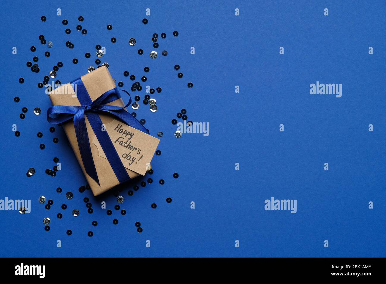 Alles gute zum Vatertag Konzept. Geschenkbox mit blauer Schleife und Konfetti auf blauem Hintergrund Draufsicht. Vorlage für Grußkarten zum Vatertag. Stockfoto