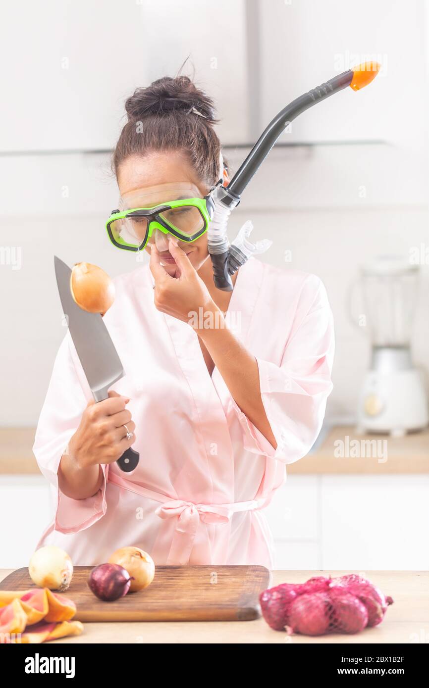 Frau trägt Schnorchel hält ihre Nase mit einer Hand Blick auf Zwiebel auf einem Messer in der anderen Hand stecken. Stockfoto