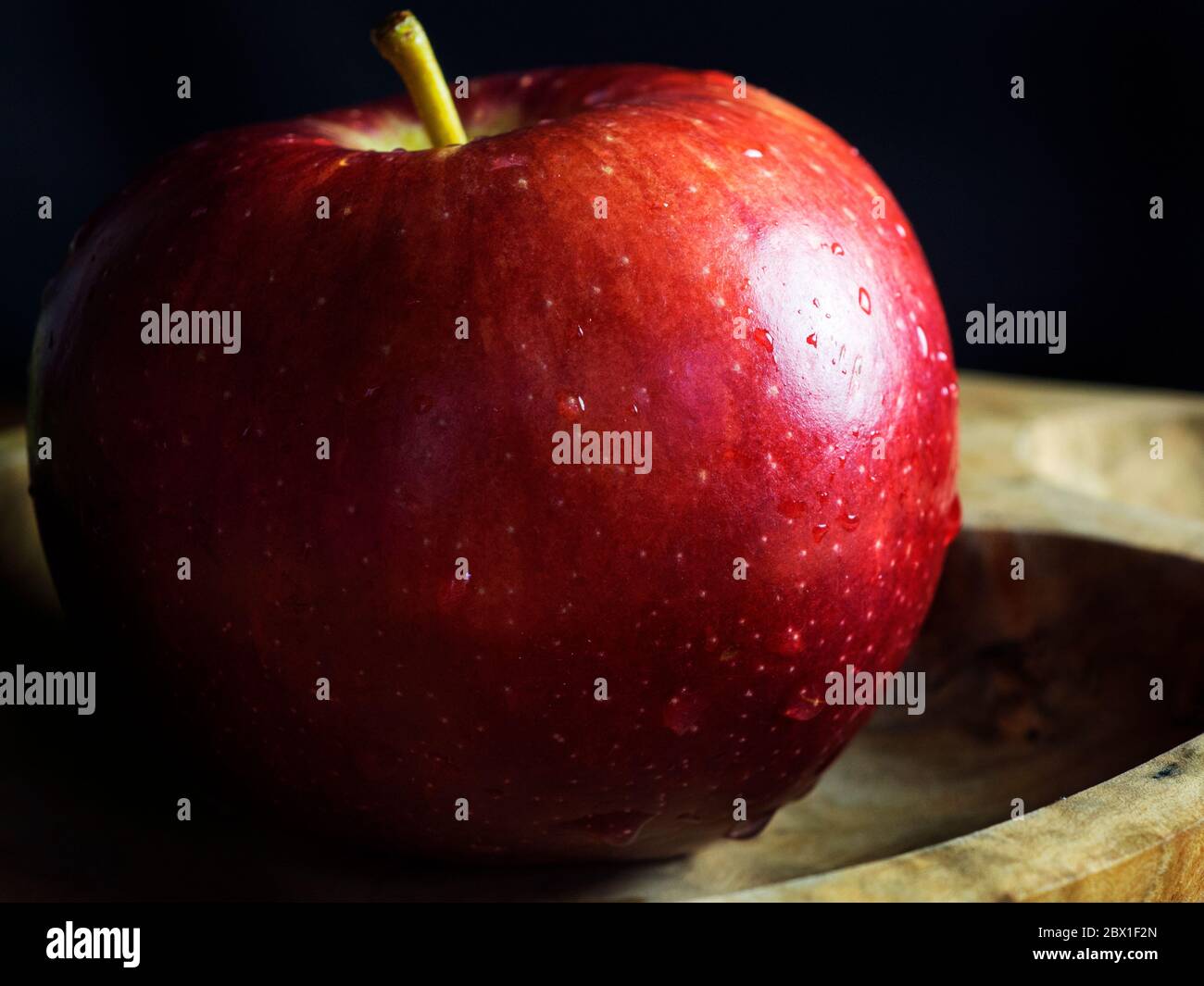 Ein einzelner Braeburn, der einen Apfel in einer Holzschale vor schwarzem Hintergrund isst Stockfoto