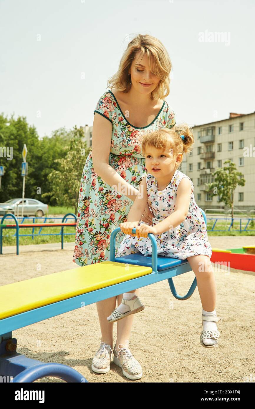 Aktives kleines Mädchen auf dem Spielplatz. Spielendes Kind mit Mutter auf einer Schaukel. Stockfoto