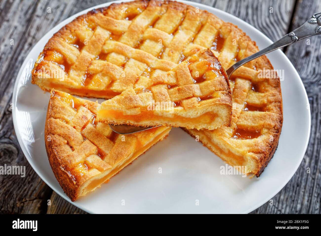 Nahaufnahme von Apricot Shortkruste Pie mit einem Gitter Pie Kruste Belag auf einer Vintage-Kuchenschaufel auf einem weißen Teller auf einem rustikalen Holztisch, Landschaft Stockfoto