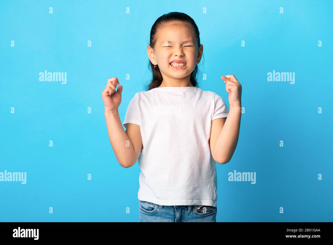 Hoffnungsvoll wenig asiatisch Mädchen, das ihre Finger kreuzt Stockfoto