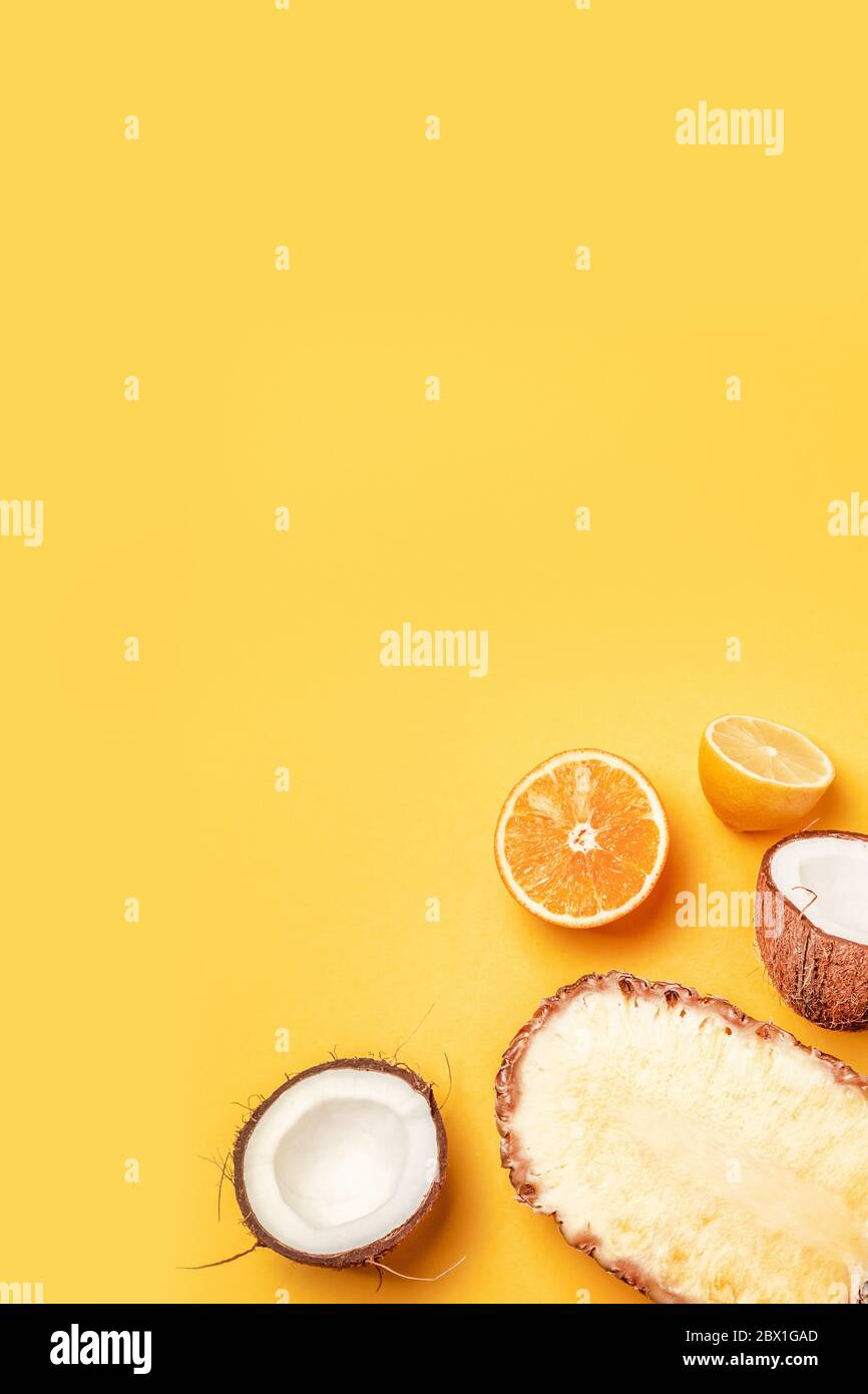 Leckere Hälften von exotischen Früchten Ananas, Kokosnuss, Orange, Zitrone auf gelbem Hintergrund. Vertikales Foto, Draufsicht mit Kopierbereich Stockfoto