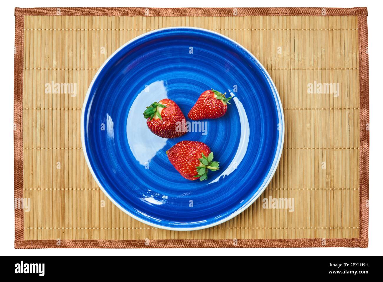 Drei rote Erdbeeren auf einem blauen Teller auf einer Zuckerrohr-Serviermatte Stockfoto