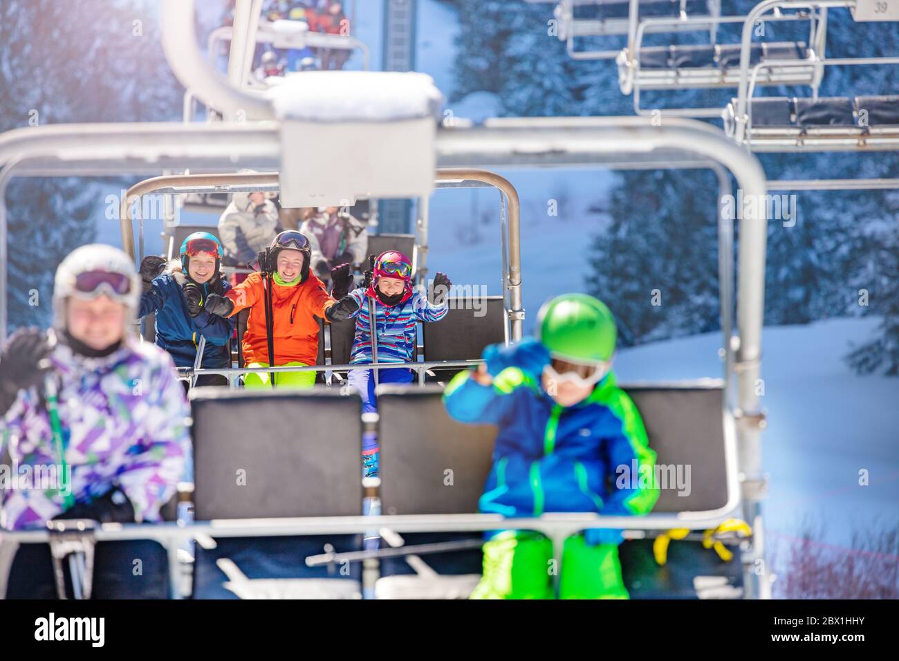 Viele Kinder Freunde sitzen auf verschiedenen Stuhl auf Skilift auf Bergort und winken Hände Stockfoto