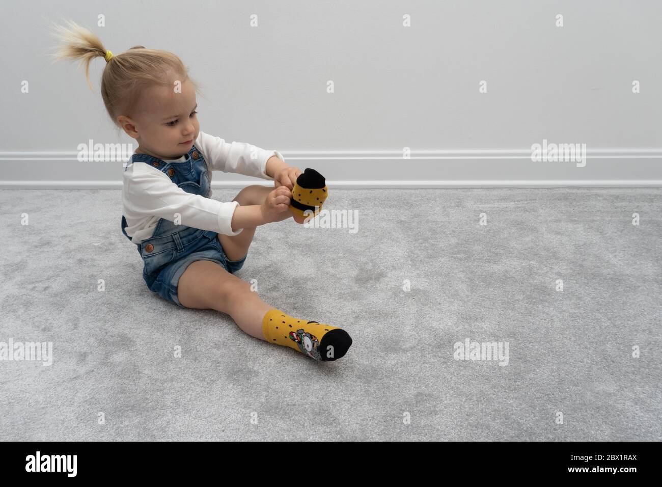 Nettes Baby Mädchen lernen, Socken zu Hause, auf dem Boden, weiße Wand hinten anziehen. Stockfoto