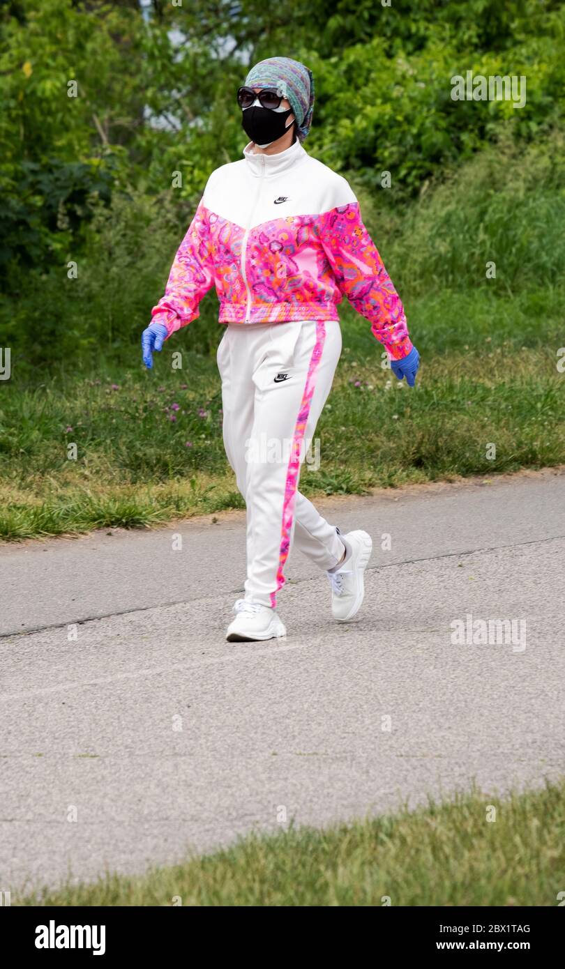 Eine asiatische Amerikanerin, die geht und ihre Operationsmaske und blaue Gummihandschuhe trägt. In Little Bay Park, Whitestone, Queens, New York. Stockfoto