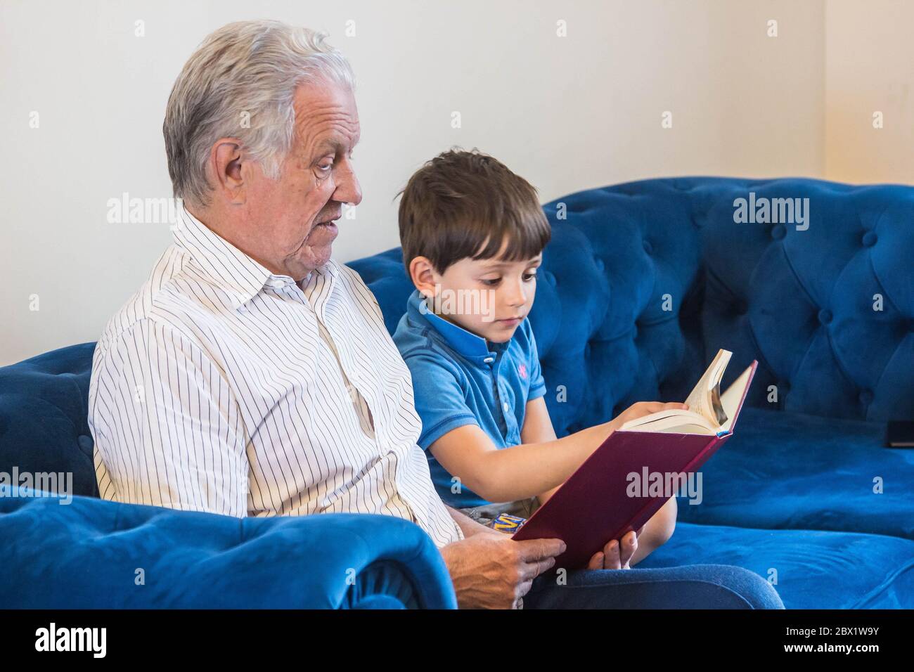 Großvater und Enkel lasen ein Buch, während sie auf dem Sofa saßen und sich entspannen Stockfoto