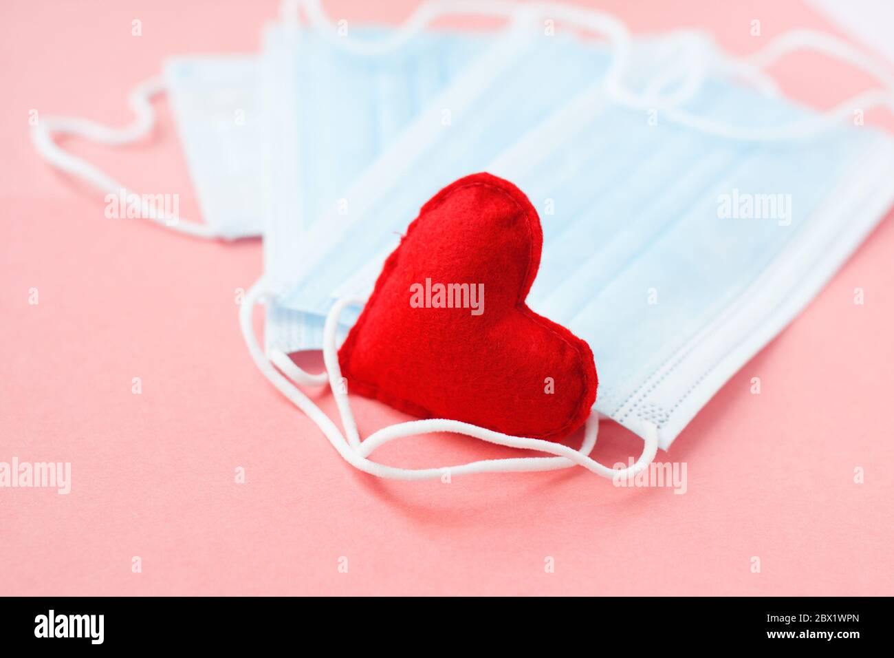 Blaue Tuch medizinische Masken mit rotem Herz auf rosa Hintergrund. Tapferes Herz und Dankbarkeit gegenüber allen Arbeitern der Medizin. Coronavirus, COVID-19, pandemische Duri Stockfoto