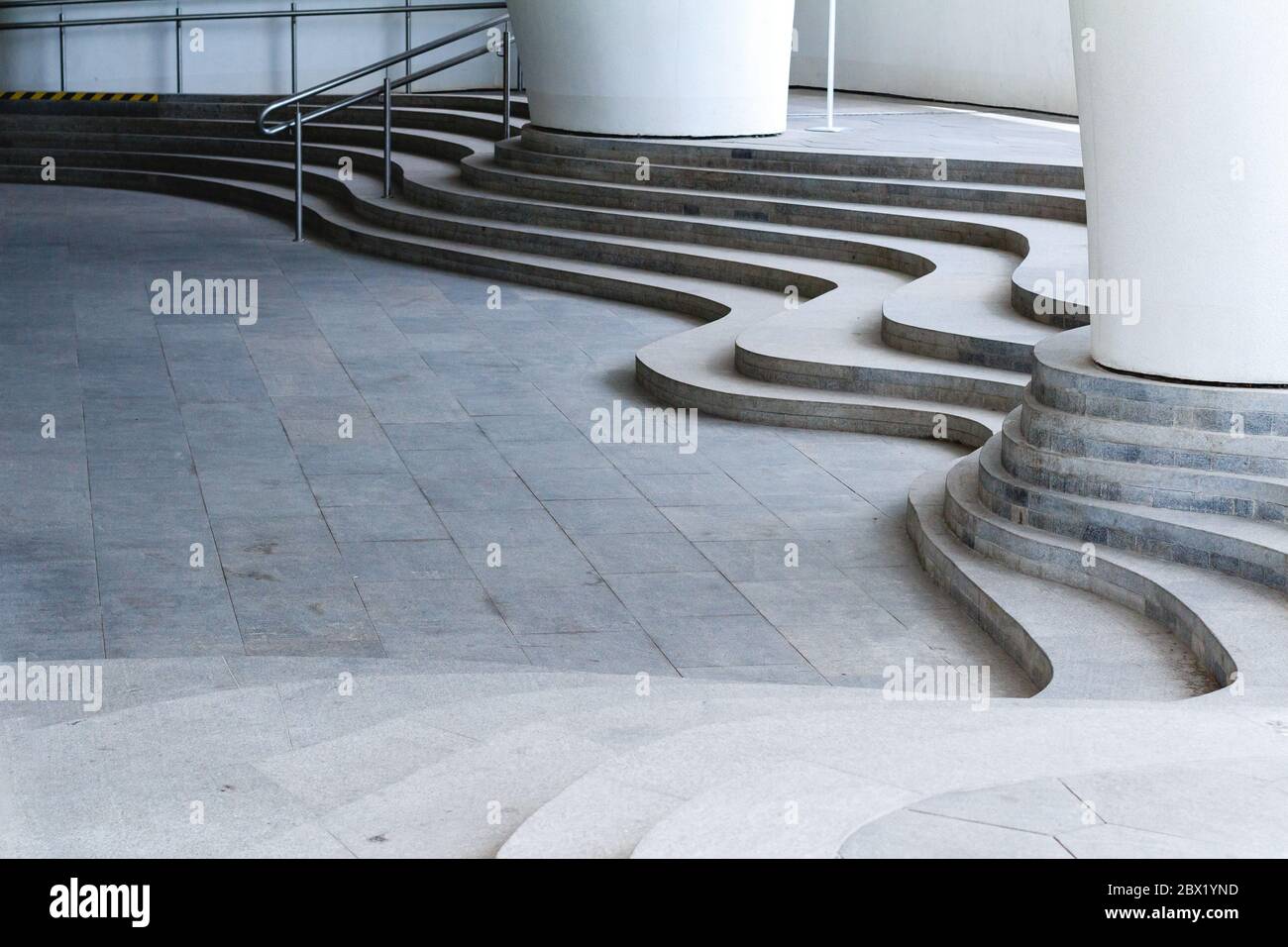 Geschwungene Treppen aus massivem grauen Stein und Säulen. Industrielle urbane abstrakte Muster Stockfoto