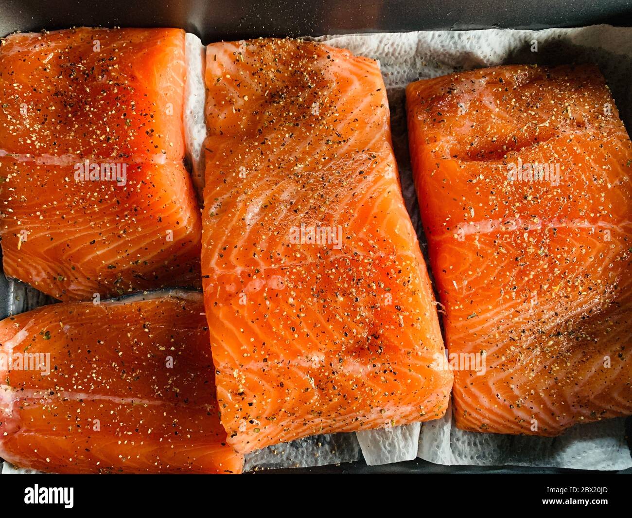 Einige Stücke Filet von rohem rotem Fisch mit Gewürzen liegen auf einem Backblech vor dem Rauchen, schwarzer Pfeffer und Salz, Lachs Stockfoto