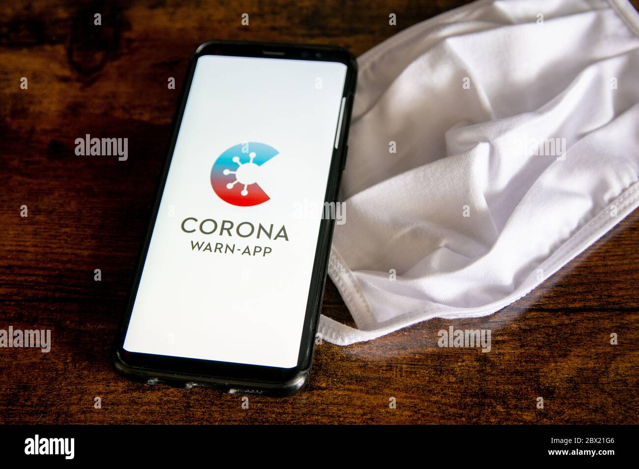 Zittau, Sachsen / Deutschland - 4. Juni 2020: Corona Virus Warn App für COVID-19 Tracing mit weißer Gesichtsmaske auf Holzfläche. Das neue normale, es Stockfoto