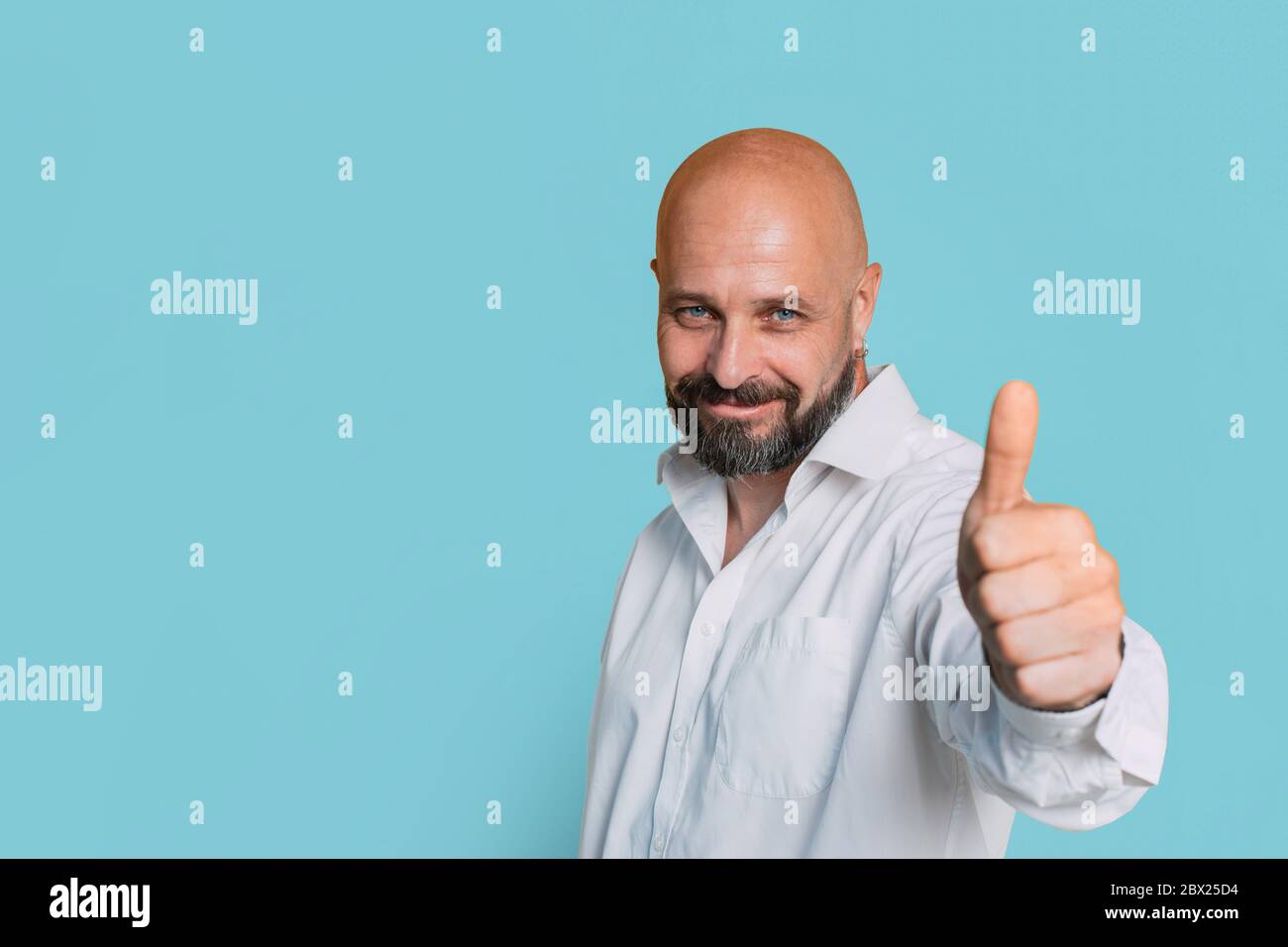 Ein schöner, ernsthafter Mann mittleren Alters in einem weißen Hemd zeigt einen Daumen bis zur Kamera auf gelbem Hintergrund Porträt eines älteren Mannes, der seinen ha aushält Stockfoto