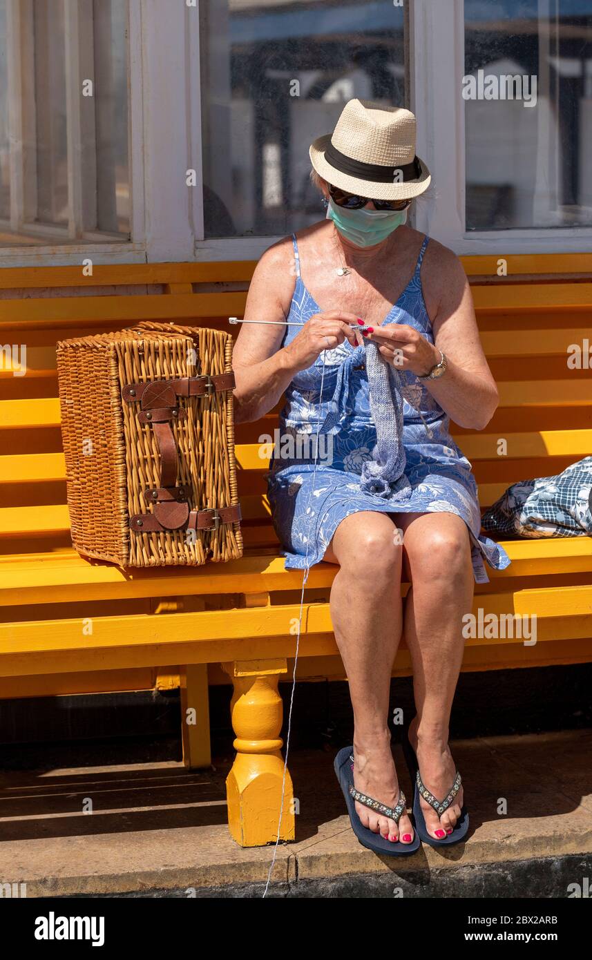 Southsea, Portsmouth, England, Großbritannien. 2020, Frau auf einer Bank am Meer, die während der Covid-19-Sperre einen Wollpullover strickt. Stockfoto