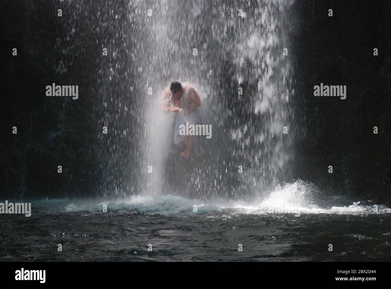 Junger Mann springt durch einen Wasserfall Stockfoto