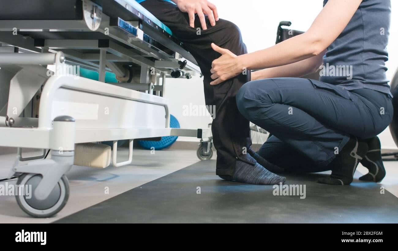 Physiotherapeut, der mit behinderten Menschen im Rollstuhl auf einem Therapietisch trainiert. Stockfoto