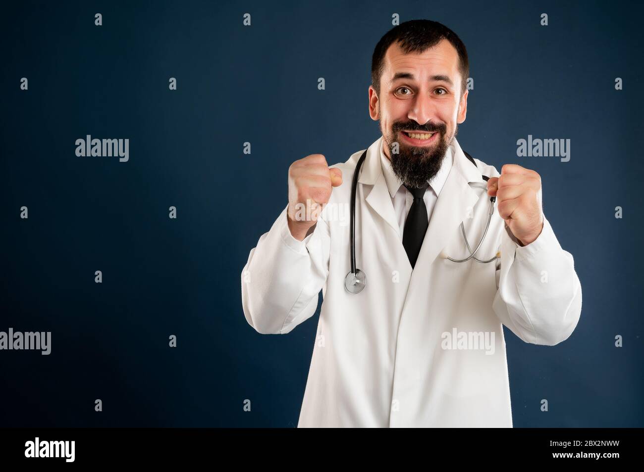 Porträt des männlichen Arztes mit Stethoskop in medizinischer Uniform hob Fäuste bis Ausrufen mit Freude und Aufregung posiert auf einem blauen isolierten Hintergrund. Stockfoto