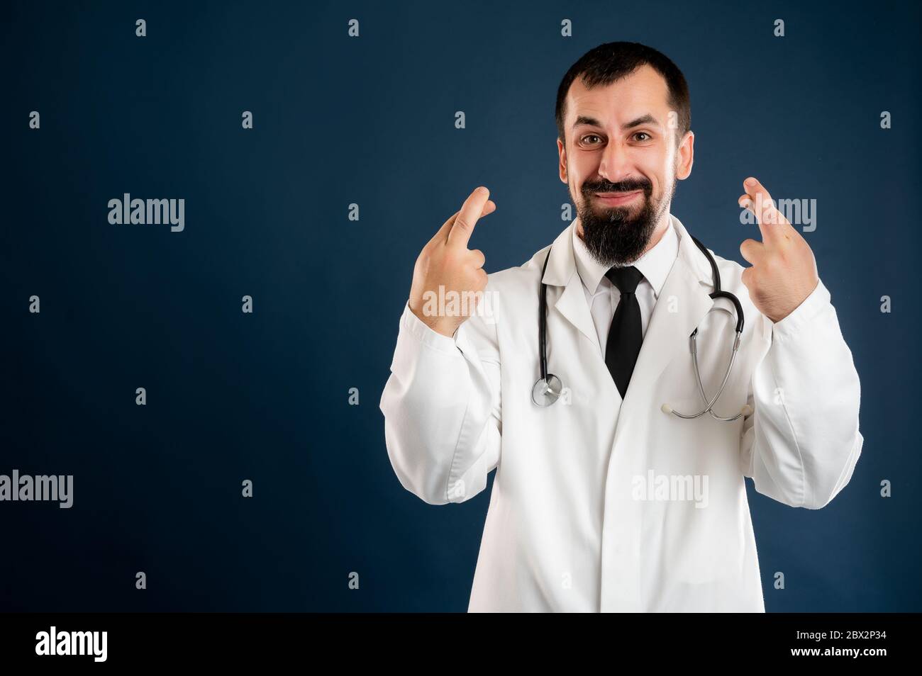 Porträt des männlichen Arztes mit Stethoskop in medizinischer Uniform zeigt doppeltes Glück posiert auf einem blauen isolierten Hintergrund. Stockfoto