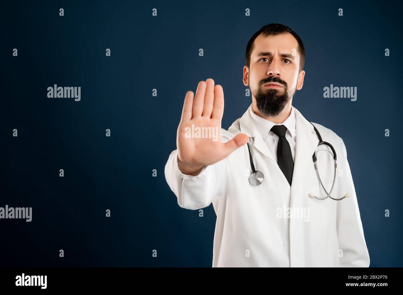 Porträt des männlichen Arztes mit Stethoskop in medizinischer Uniform mit Stoppschild posiert auf einem blauen isolierten Hintergrund. Stockfoto