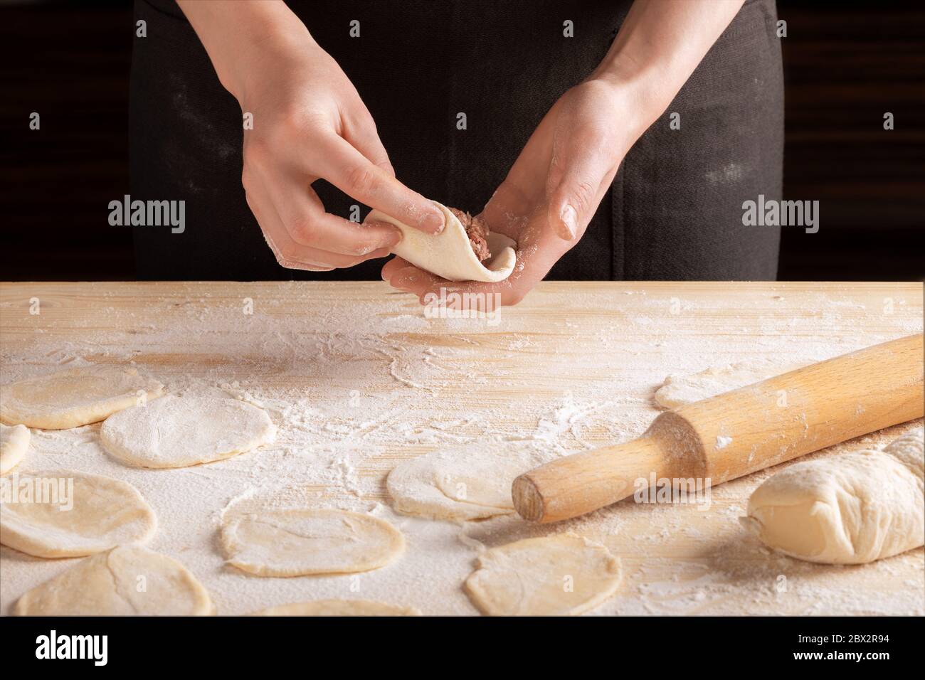 Vorderansicht der Hände der Frau, die Fleischknödel mit Holz-Nudelholz machen. Der Prozess der Herstellung von hausgemachten Knödeln, Schritt 10. Hackfleisch auf Teig, die Stockfoto
