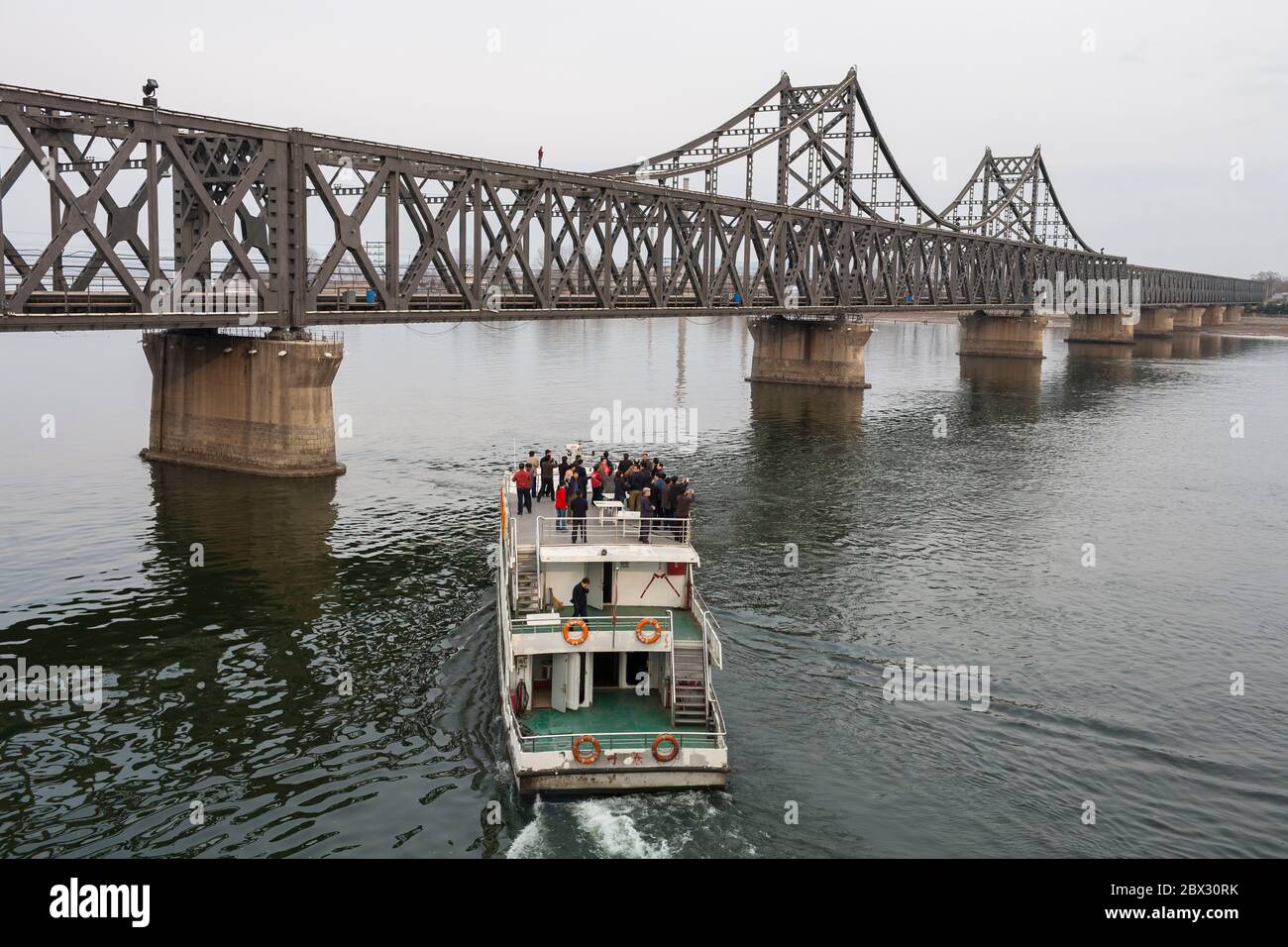 China, Provinz Liaoning, Stadt Dandong, chinesisch-koreanische Freundschaftsbrücke, Touristenboot, das sich dem nordkoreanischen Ufer des Yalu nähert, Lastkraftwagen, Personenzüge und Arbeiter überqueren diese Brücke täglich Stockfoto
