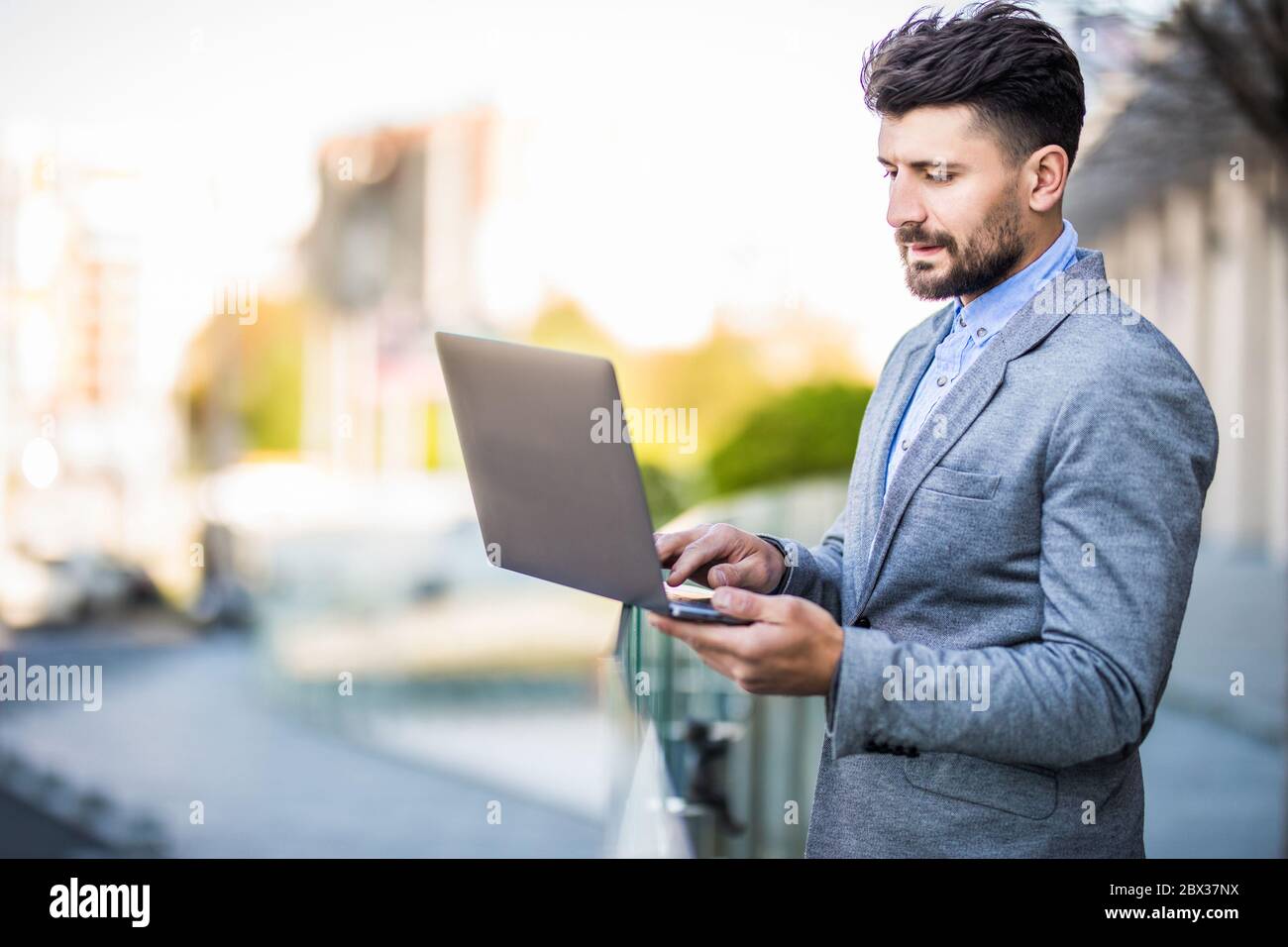 Ein schöner Geschäftsmann sitzt neben seinem Laptop auf der Straße Stockfoto