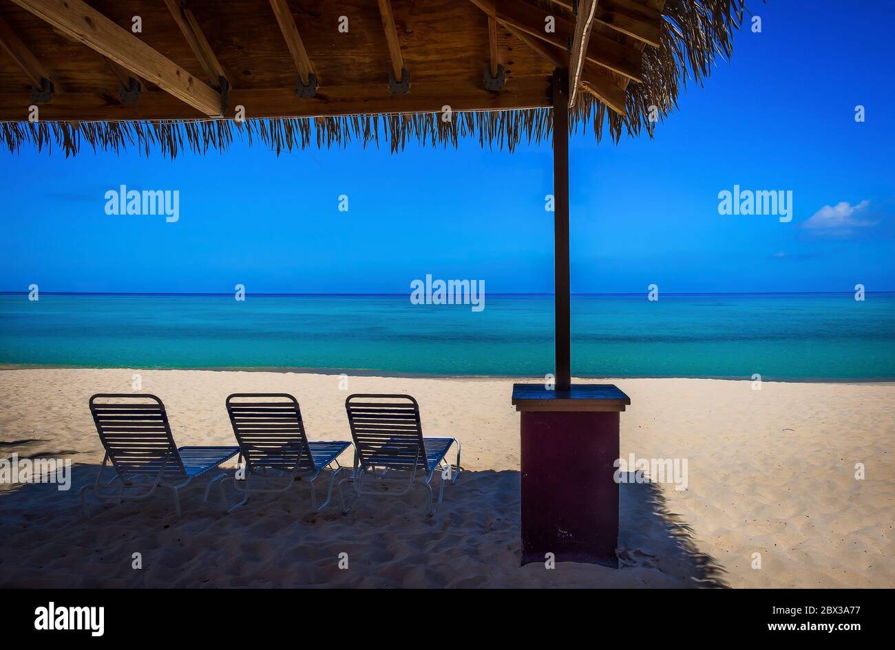 Sonnenliege Stühle unter einer Hütte auf einem leeren Seven Mile Beach in der Karibik während der Gefangenschaft, Grand Cayman, Cayman Islands Stockfoto