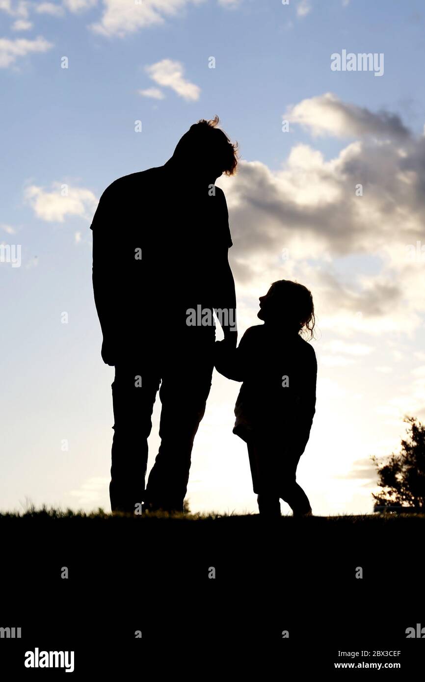 Eine Silhouette eines süßen Moments zwischen einem Vater und seinem kleinen Mädchenkind, das die Hände hält und bei Sonnenuntergang draußen zusammenläuft. Stockfoto