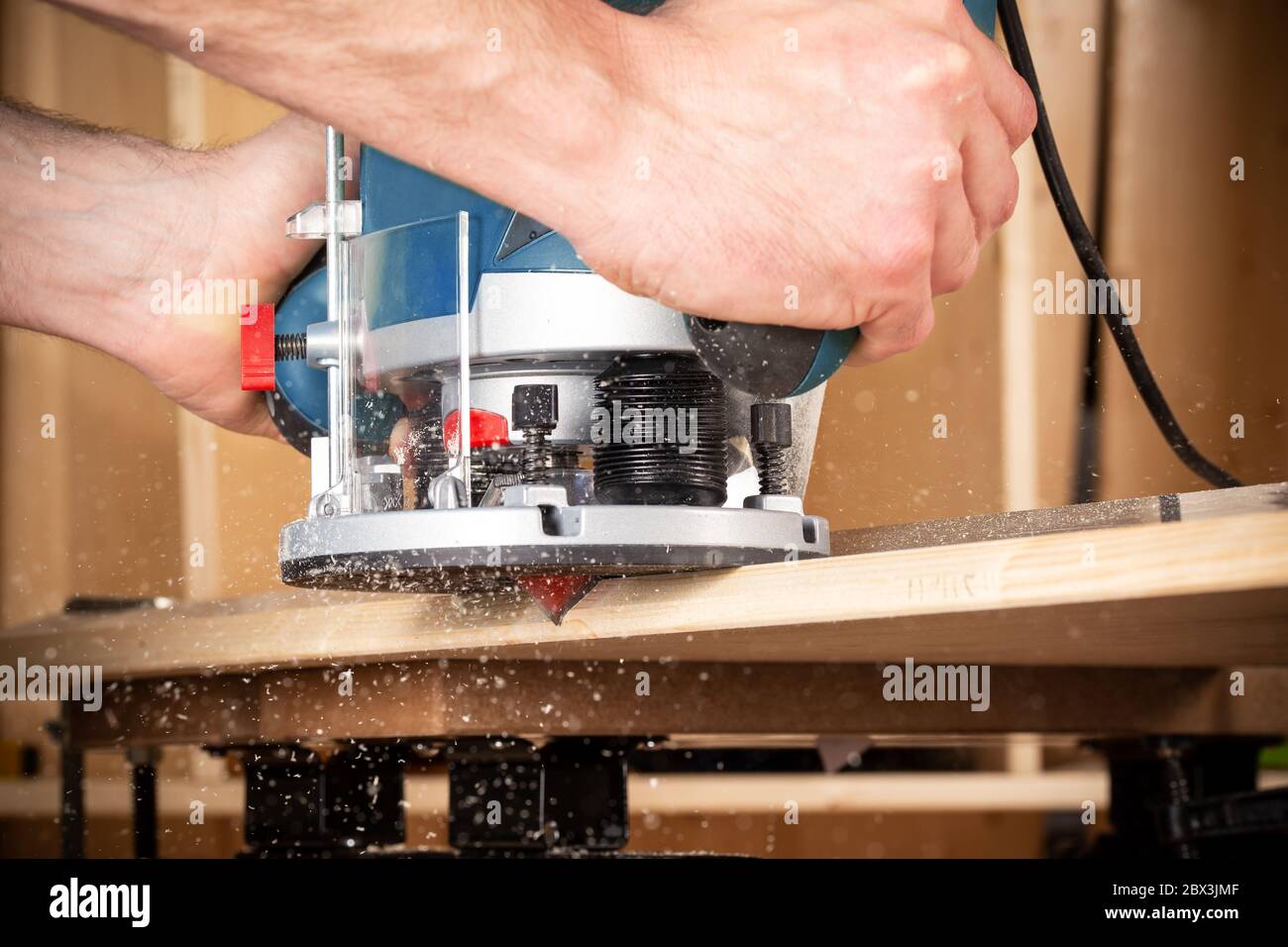 Nahaufnahme von Tischler mit Hand Holz Fräser Maschine bei der Arbeit. Nahaufnahme von Fräsen einer Fase in Planke aus Kiefer Holzbearbeitung Bauwerkzeug Konzept furnit Stockfoto