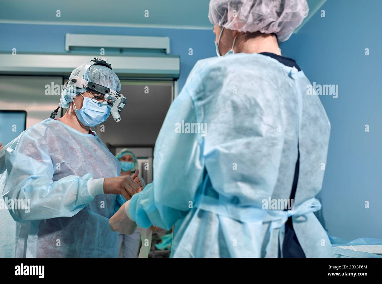 Ein Team von Chirurgen bereitet sich auf die Operation vor. Chirurgen tragen sterile Kleidung vor der Operation mit Hilfe von Krankenschwestern, sterile Kleider, Handschuhe, Masken, in Stockfoto