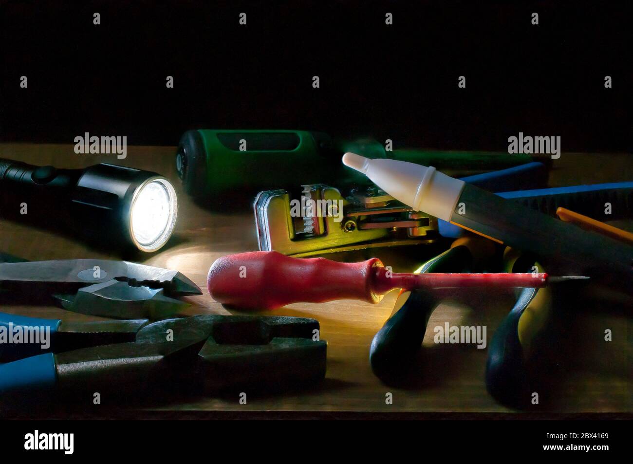 Elektriker Werkzeuge an einem dunklen Ort, beleuchtet von einer Taschenlampe, Schraubendreher Zange Drahtstreifen, Spannungsprüfer auf einem Tisch. Stockfoto